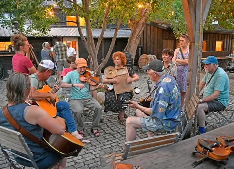 A group of people playing music outdoors on instruments including guitars, a violin, and a washboard.