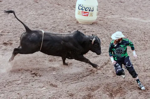 A bullfighter runs in an arena away from a charging black bull.