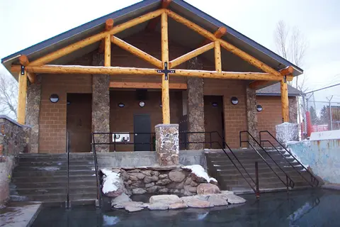 An exterior view of a rustic bathhouse with stone columns and log framing.