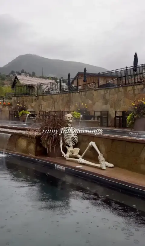 A skeleton lounging by a swimming pool on a rainy day.