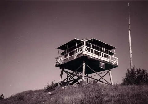 A historical photograph of a wooden lookout tower standing on a hill.