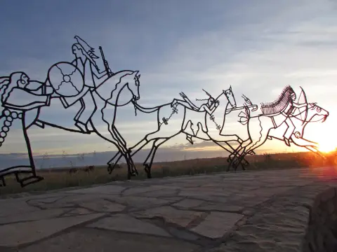 A metal sculpture of figures on horseback against a sunset sky.