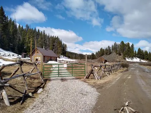 A log cabin and a gate stand in a snowy mountain landscape.