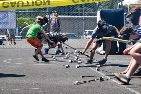 People participating in an outdoor archery activity, grabbing arrows on the ground.