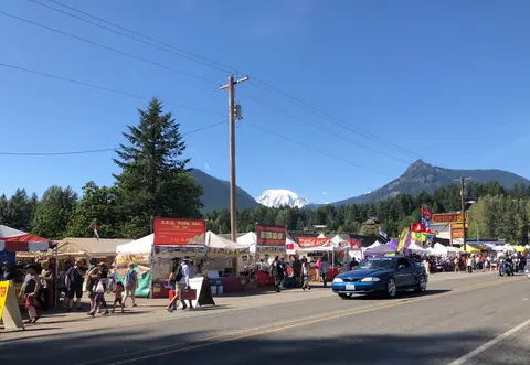 A street market with food booths and a snow-capped mountain in the background.