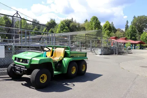 A green utility vehicle parked on pavement outside a fenced enclosure.