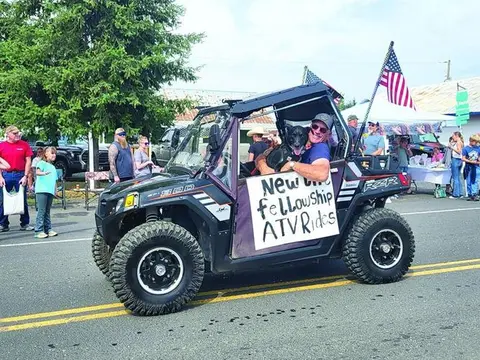 A man with a dog in an ATV during a parade.