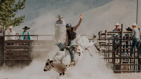 A cowboy rides a bucking bull at a rodeo while spectators watch.