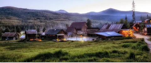 A scenic view of rustic cabins nestled in a valley with mountains in the background.