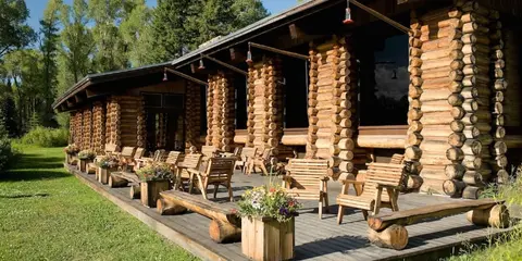 A large log cabin with a wooden porch and chairs.