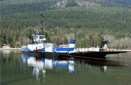 A cable ferry on a body of water with wooded hills in the background.