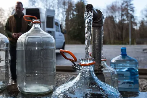 Water pours from a pipe into a glass jug outdoors.