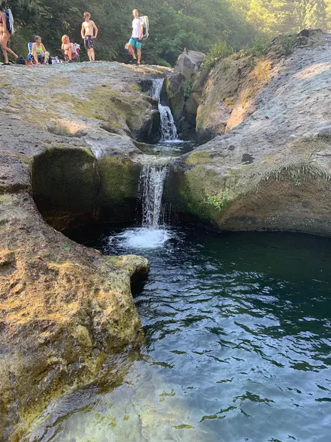A rocky waterfall flowing into a pool with people relaxing nearby.