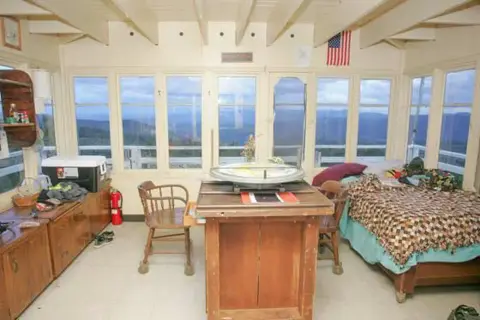 An interior view of a room with a bed and a view outside through large windows.