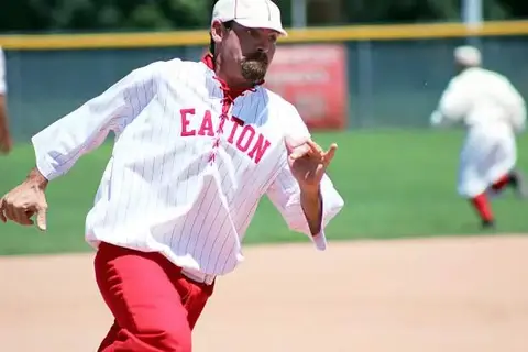 A baseball player in a vintage uniform runs on the field.