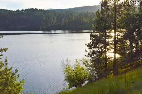 A calm lake surrounded by forested hills under a bright sky.