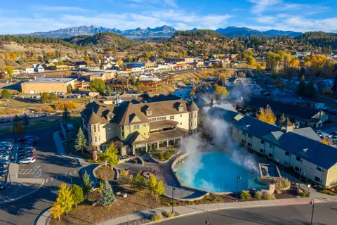 Aerial view of a hot springs resort with steaming blue water pools and a town in the background.