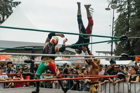 Wrestlers perform in a ring outdoors before a crowd.