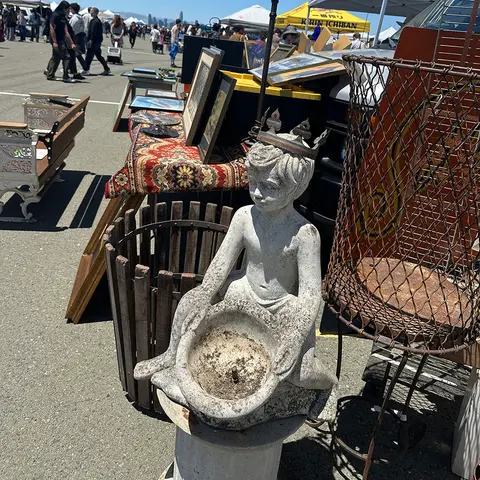 A concrete statue of a small figure holding a basin is displayed at an outdoor market.