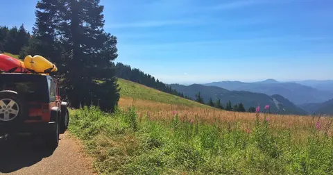 A vehicle parked on a mountain road overlooking a scenic valley under a blue sky.