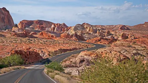 A winding road snakes through a desert landscape with red rock formations under a cloudy sky.