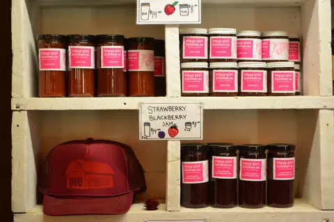A photo showing shelves stocked with jars of jam and a hat.