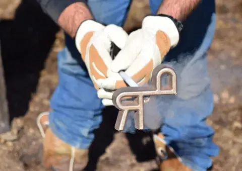 A person wearing gloves holds a metal branding iron.