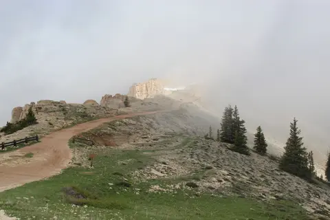 A dirt road winds along a mountain ridge covered in fog.