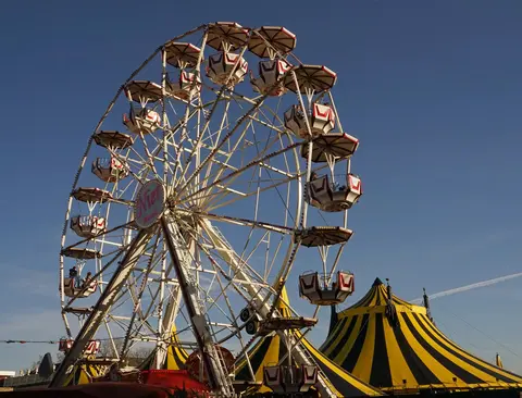 A large Ferris wheel stands against a clear blue sky with a striped tent below.