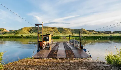 A cable ferry docked at a riverbank with hills in the background.