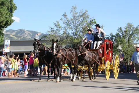 A stagecoach pulled by three horses travels down a street during a parade.