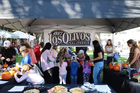 People at a booth decorated with a banner at an outdoor event.