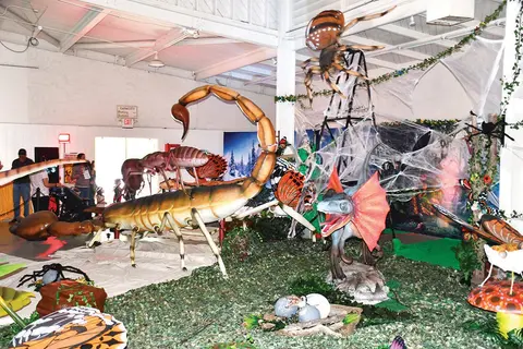 An indoor exhibition featuring large models of insects and a dinosaur.