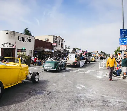 A parade with classic cars moving down a town street lined with spectators.