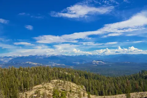 A scenic view of a forested mountain landscape under a bright blue sky with scattered clouds.