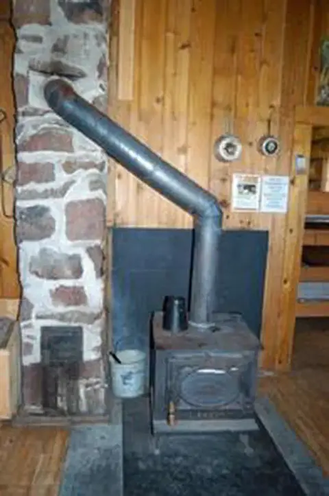 A wood-burning stove with a metal pipe inside a wooden room.