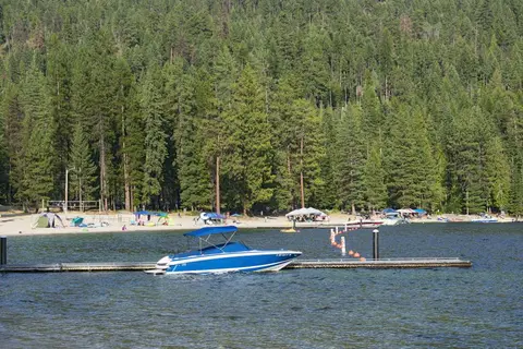 A blue motorboat docked at a pier on a lake with a forested shoreline in the background.