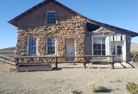 An old stone and adobe building with a wooden fence in front under a clear blue sky.