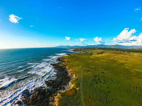 An aerial view of a rugged coastline meeting a vast blue ocean under a partly cloudy sky.