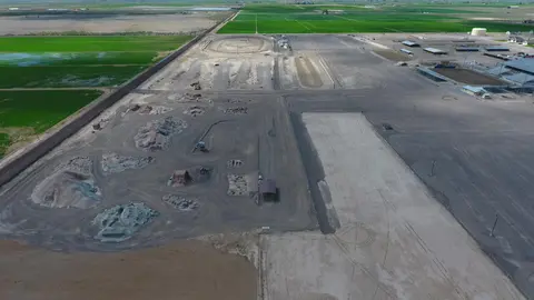An aerial view shows a large dusty outdoor area surrounded by agricultural fields.