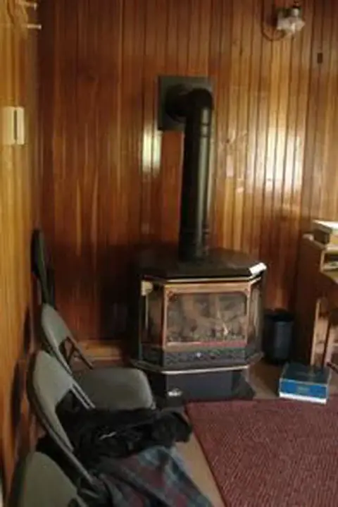 A wood-burning stove is placed in front of wood-paneled walls in a room.
