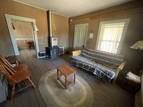 Interior view of a rustic living room with wooden floors, a couch, and a small stove.
