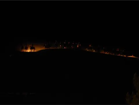 Silhouettes of riders on horseback atop a hill at night.
