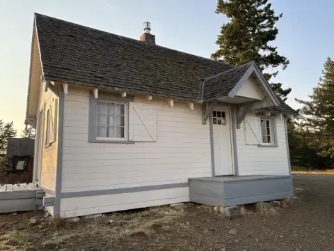 A small white building with gray trim and a shingled roof.