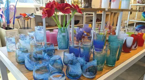A display of colorful blown glass items and flowers on a table inside a shop.