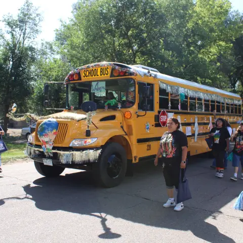 A decorated school bus drives down a street as part of a parade.
