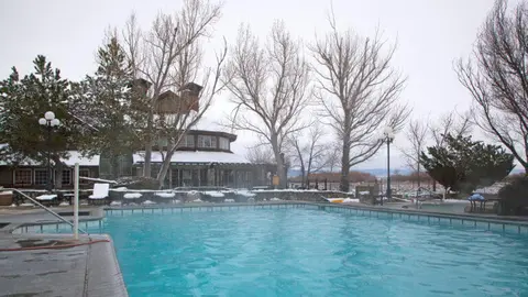 An outdoor swimming pool surrounded by snowy grounds and bare trees in winter.