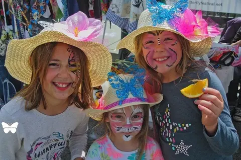 Three young girls with face paint and decorated straw hats smile for the camera.