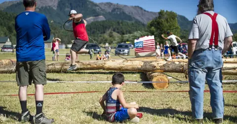 Competitors run and jump across rolling logs in a logging sports event.