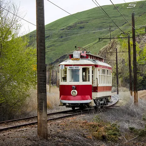 A red and white streetcar travels along tracks in a grassy, hilly landscape.